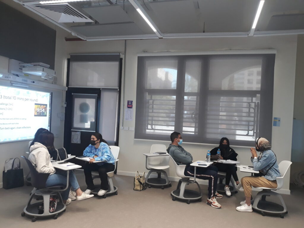 classroom with students seated facing each other talking in small groups